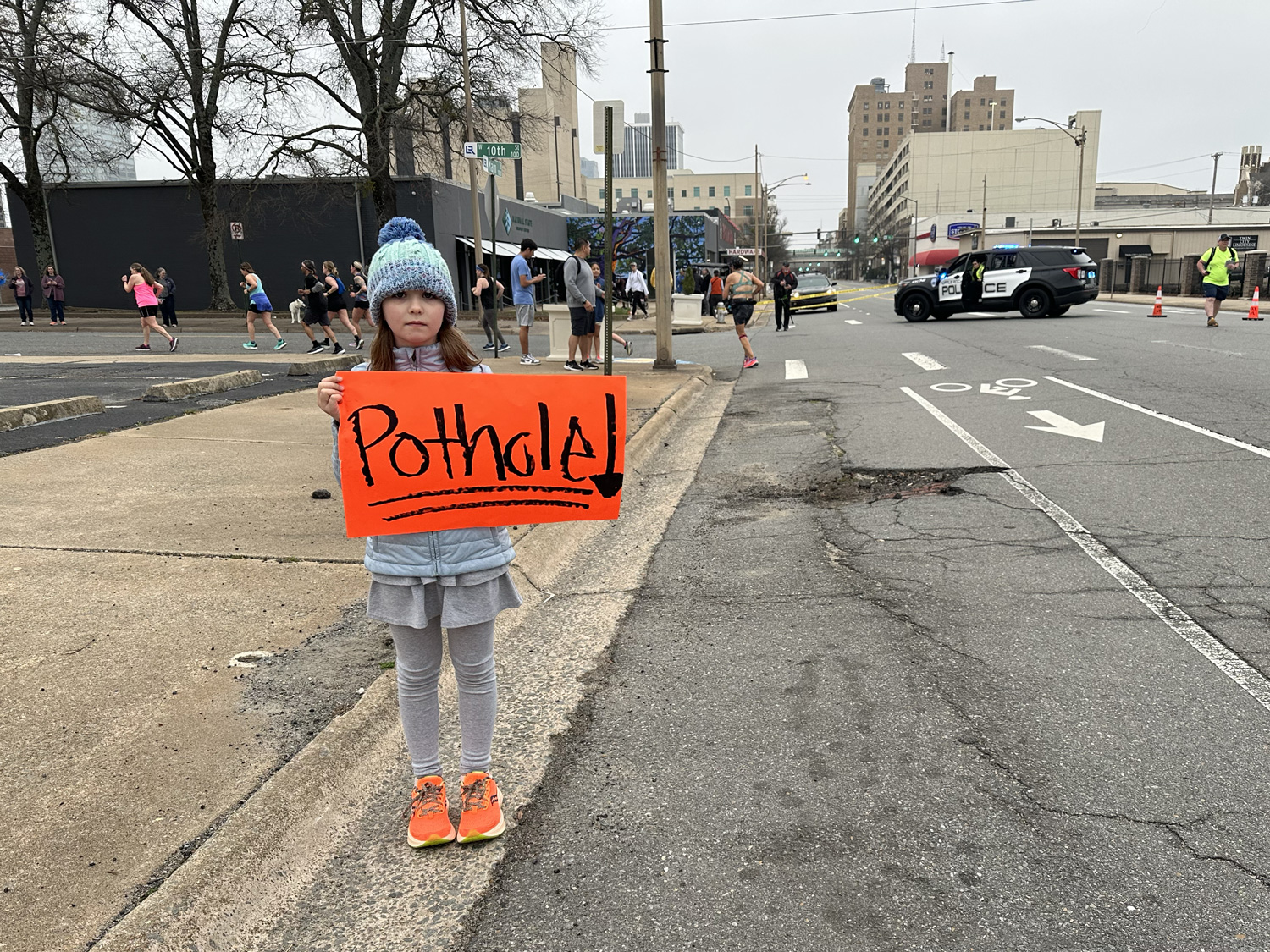 Spectator holding a "Pothole!" sign next to a pothole