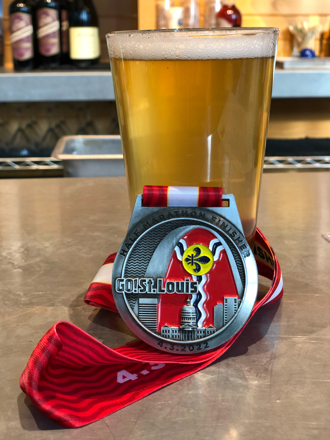 2022 GO! St. Louis half marathon medal against a pint of beer