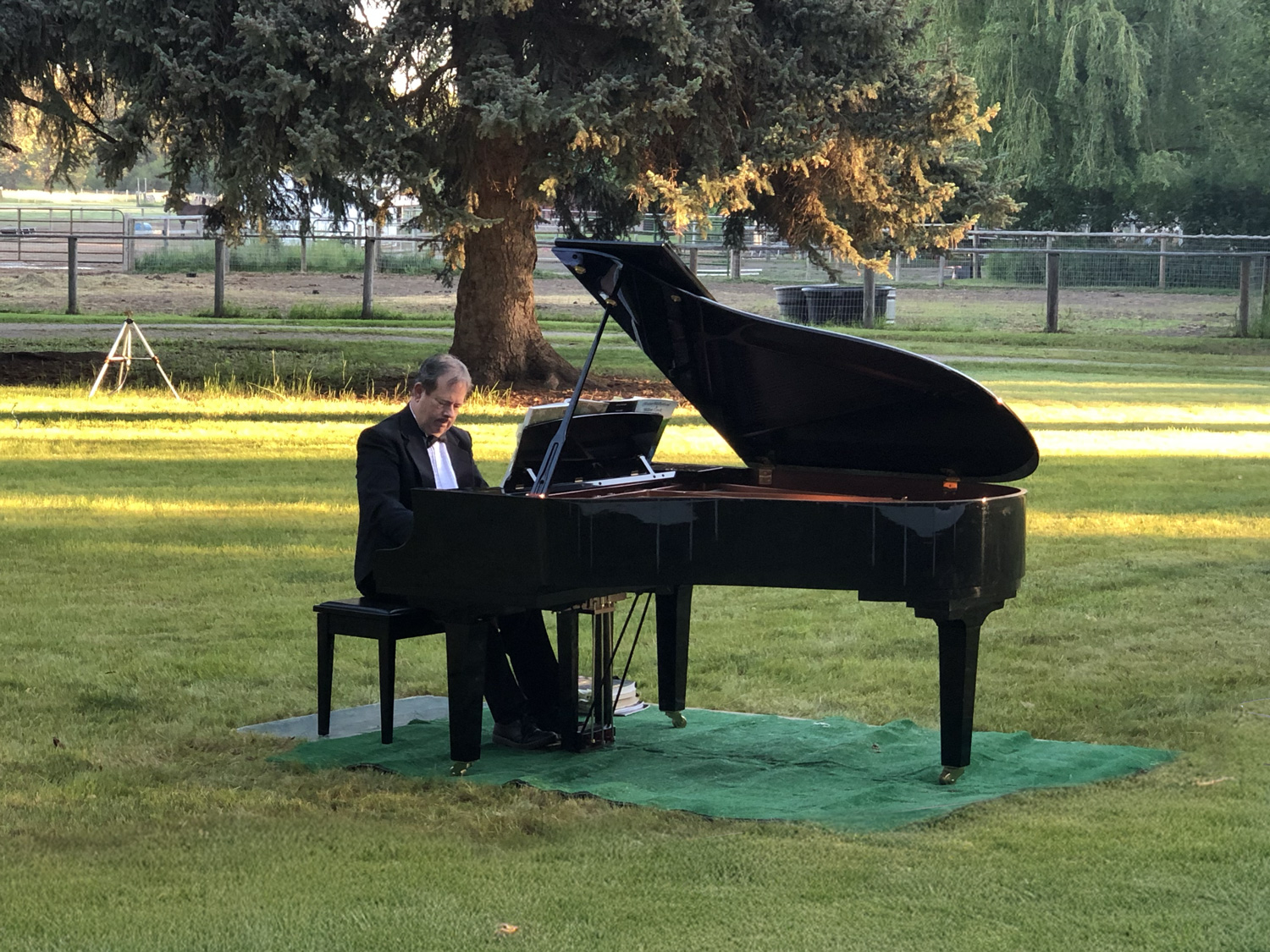 A man in a tux playing a grand piano on his lawn