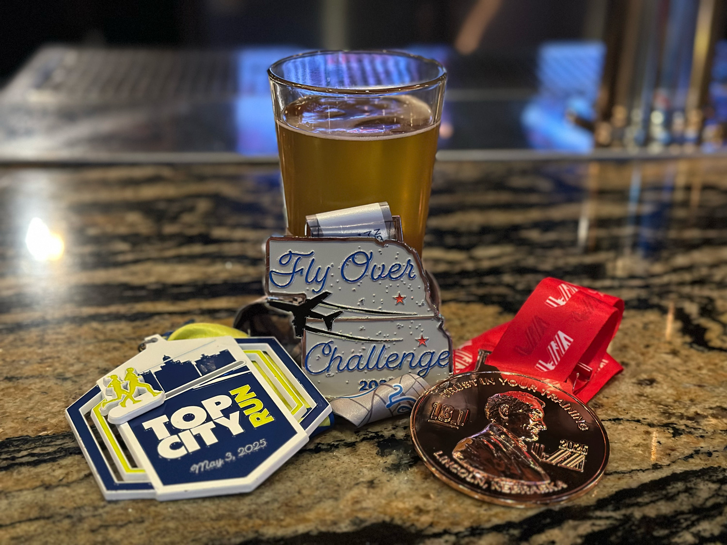 2025 Flyover Challenge medals against a pint glass of beer